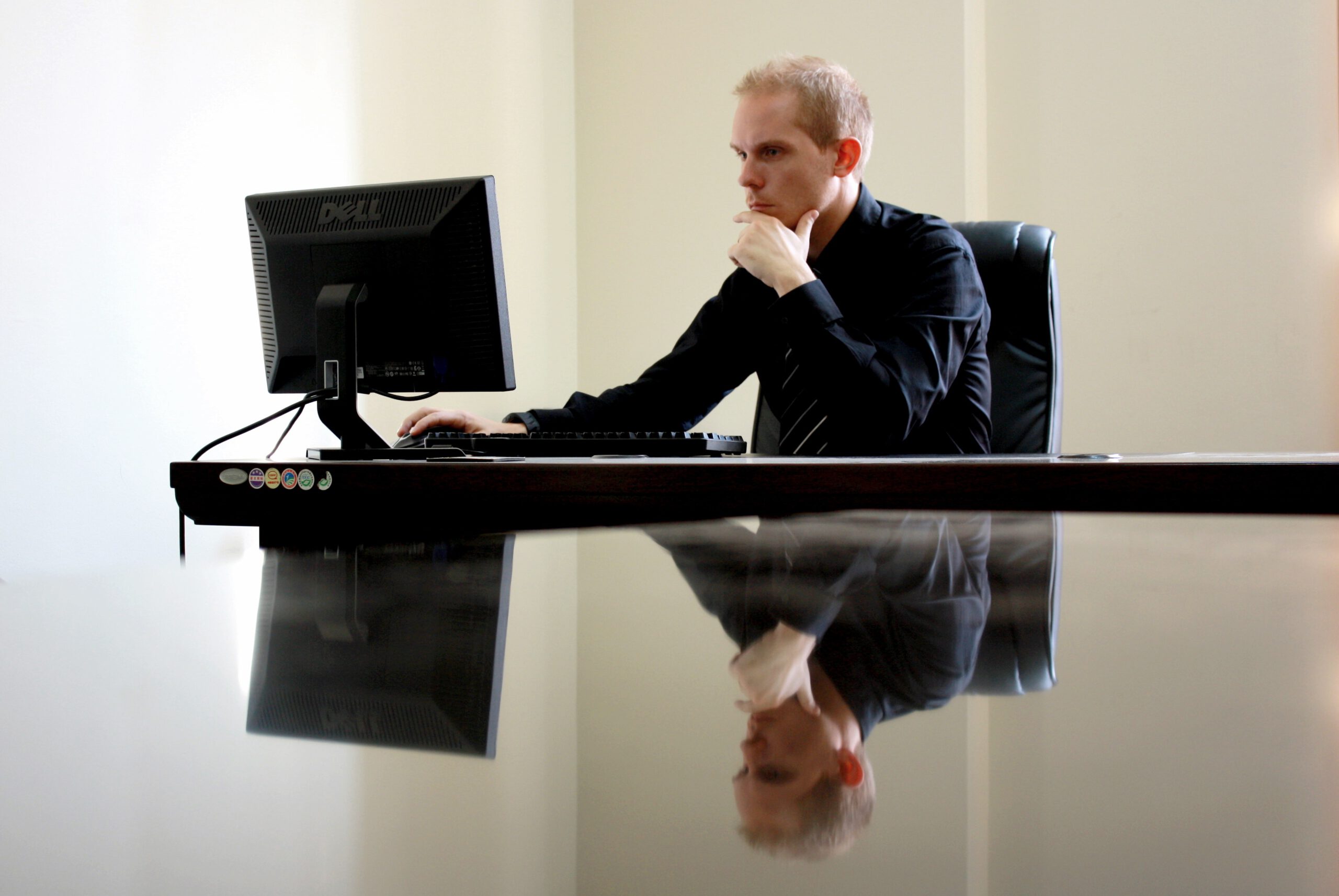 Mężczyzna siedzący przy biurku przed komputerem i zastanawiający się nad sprzedażą firmy
